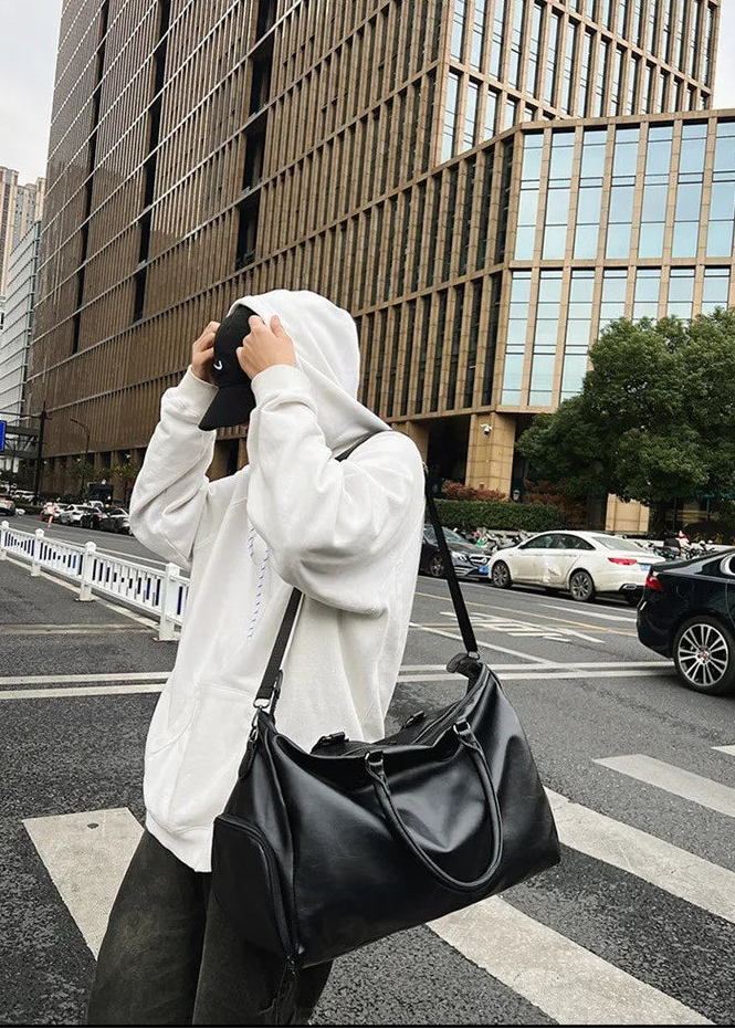 Person in a white hoodie and black pants crossing a street with a large building in the background