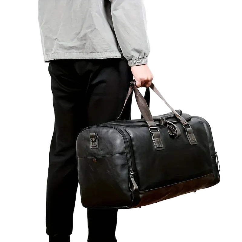 Person holding a black leather duffel bag against a white background