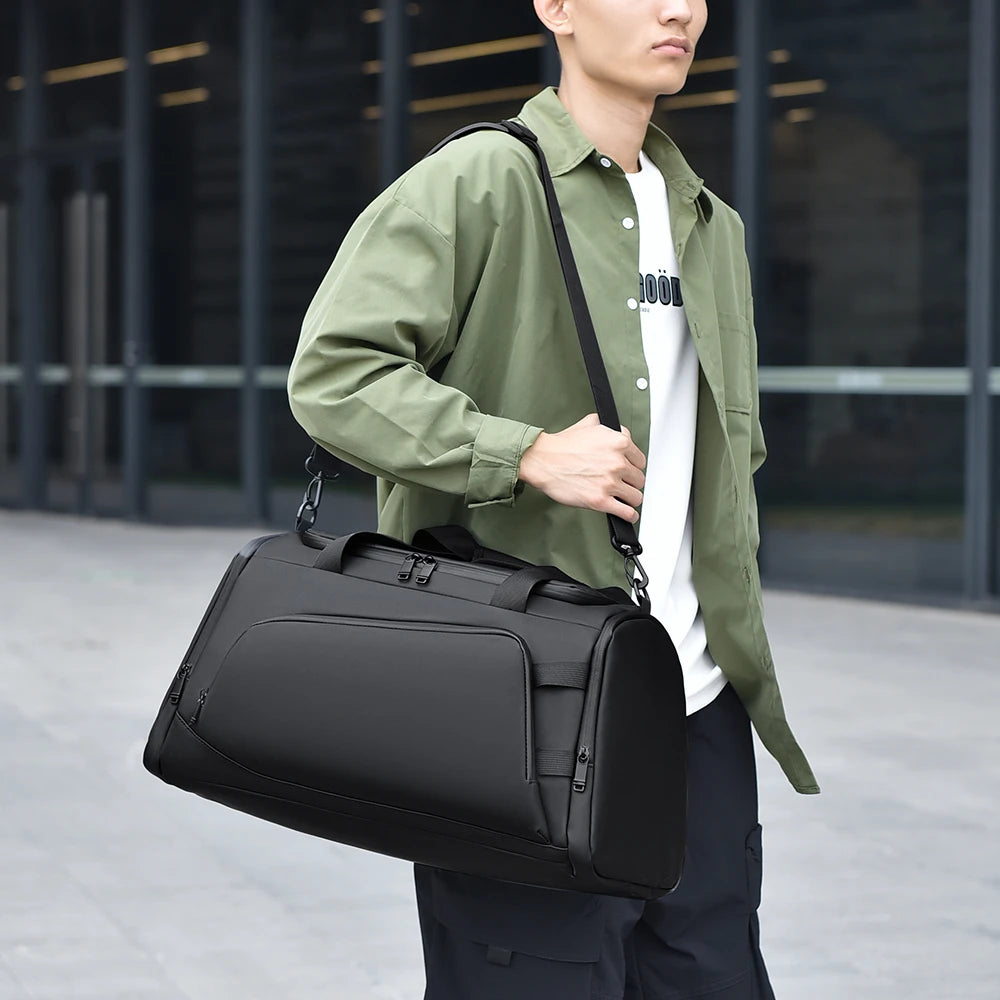 Person holding a black duffel bag outdoors