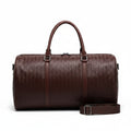 Brown textured duffel bag held over a white suitcase by a person wearing a beige coat.