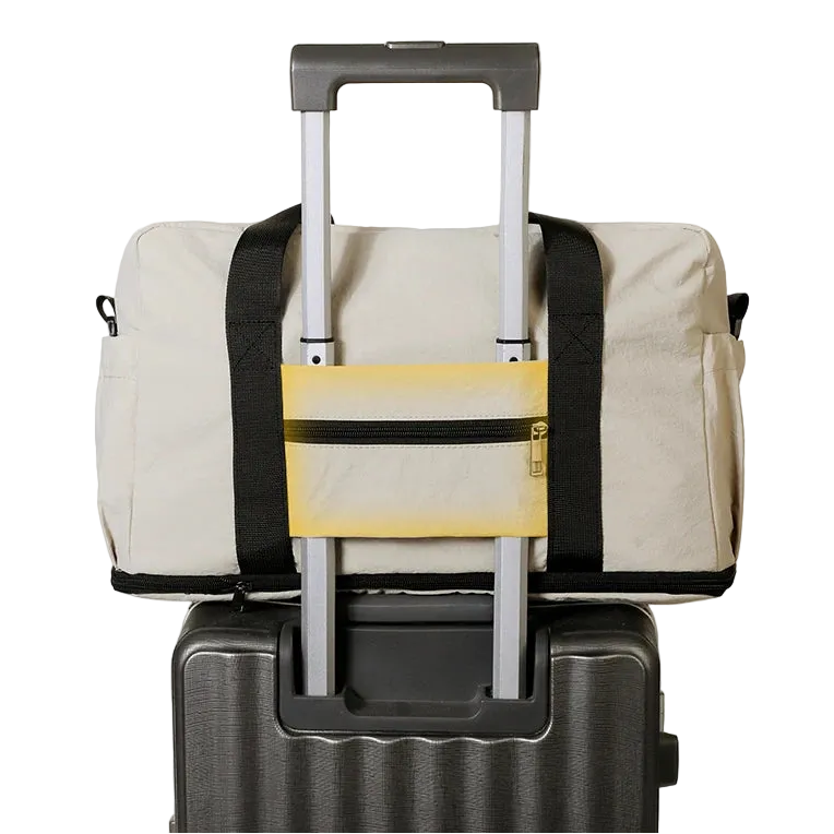 Beige duffel bag with black straps attached to a suitcase on a white background