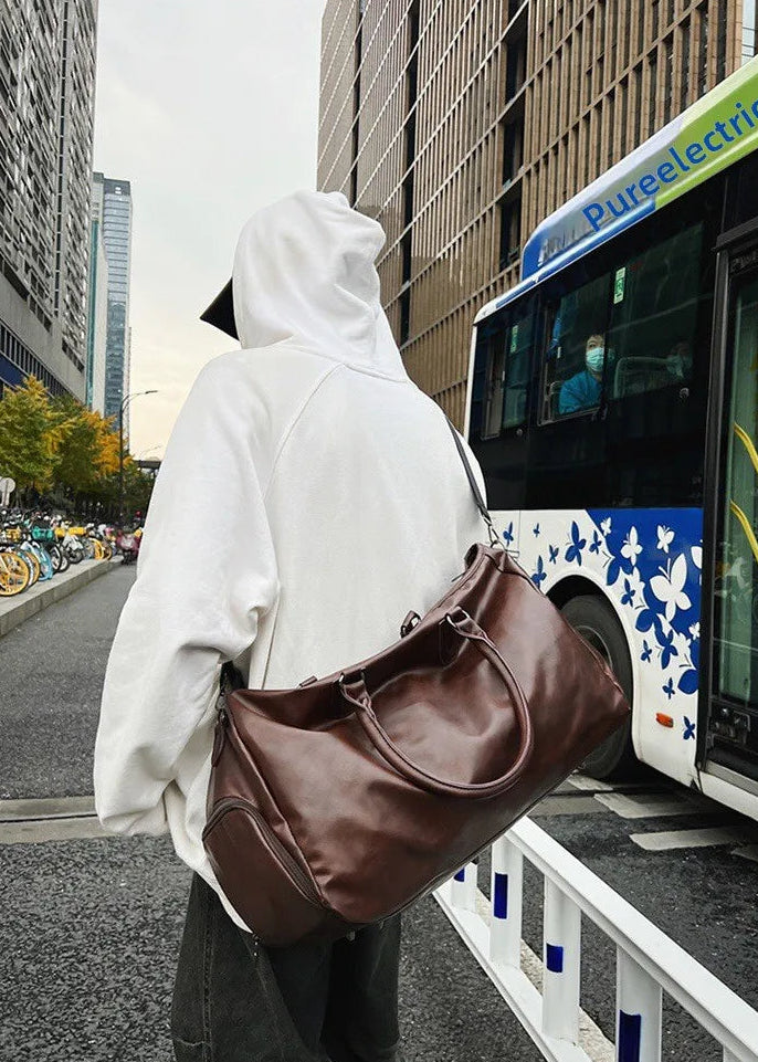 Person in a white hoodie and brown bag walking past a bus in an urban setting