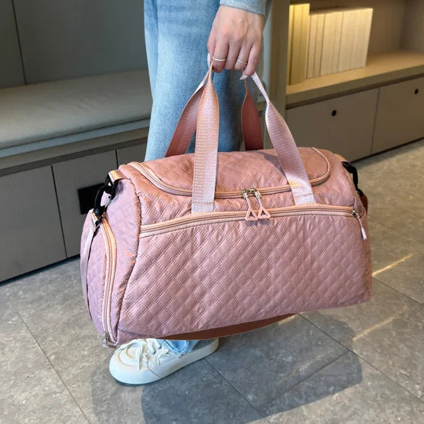 Person holding a pink quilted duffel bag in an indoor setting