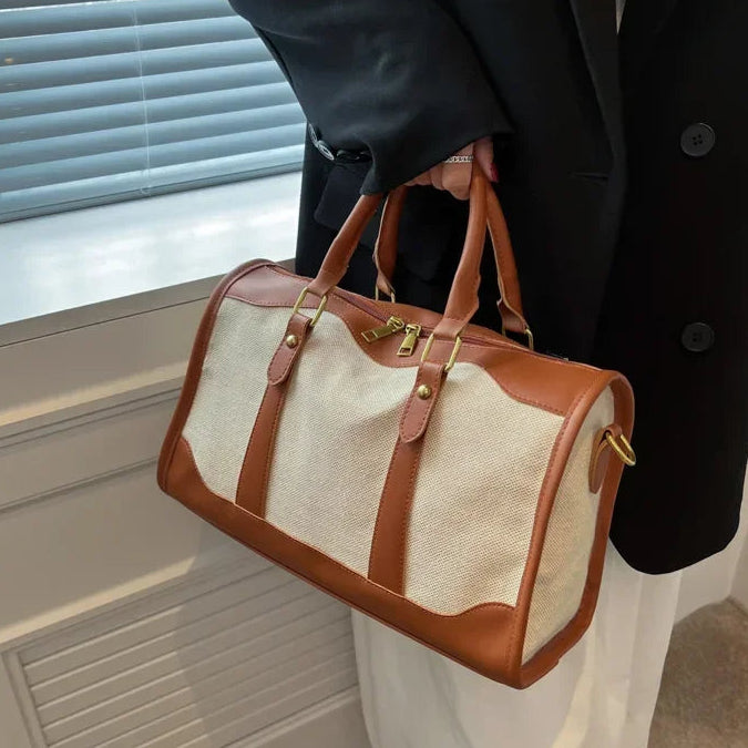 Person holding a brown and beige duffel bag in front of a window.