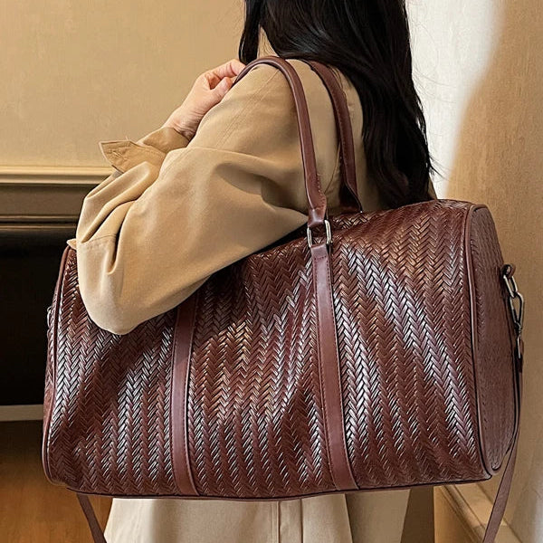 Person holding a brown woven duffel bag indoors