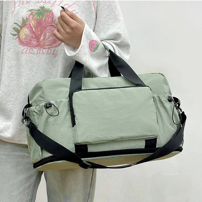 Person holding a light green duffel bag with black straps on a plain background