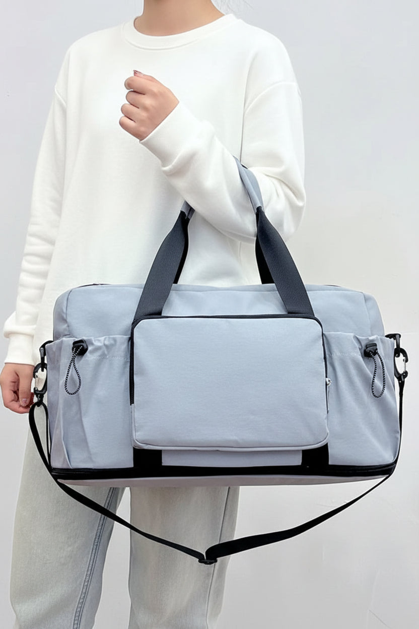 Person holding a gray duffel bag with black straps on a plain background