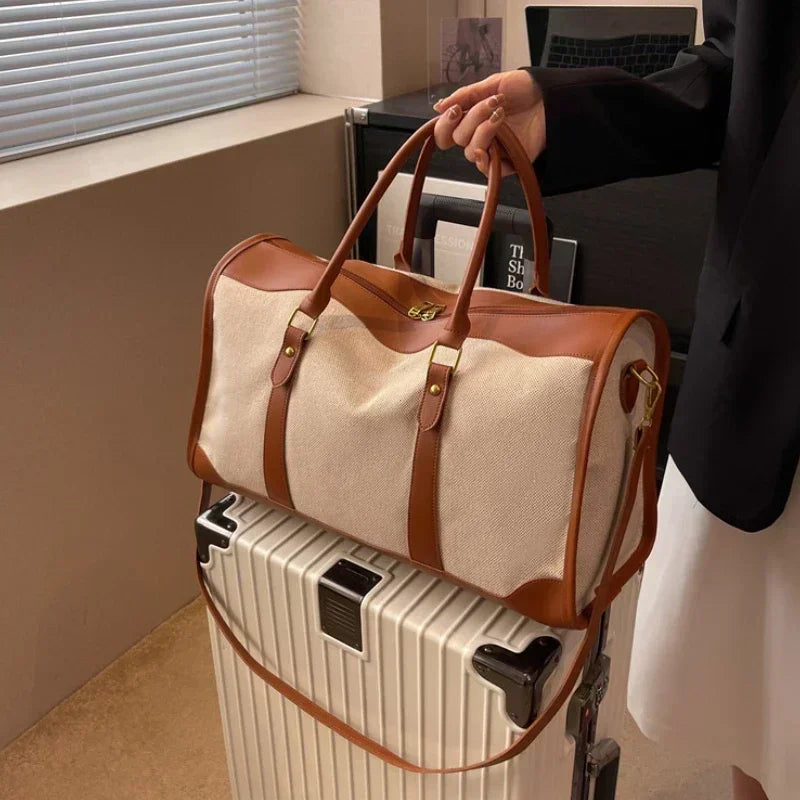 Person holding a beige duffel bag over a white suitcase in an indoor setting.