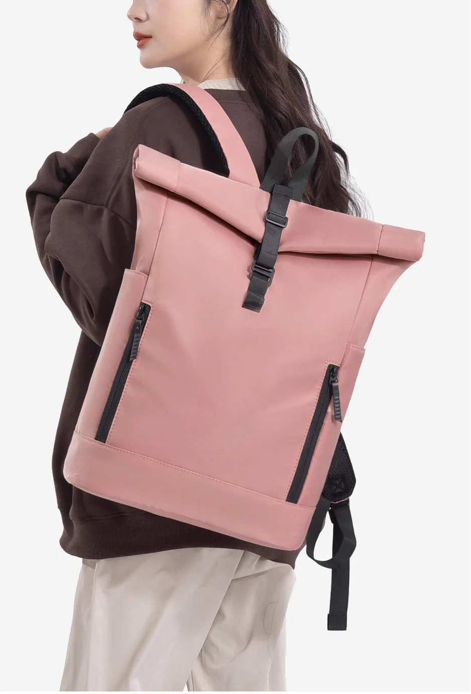 Person wearing a pink roll-top backpack with black zippers on a white background