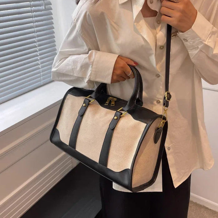 Person holding a beige and black handbag indoors.